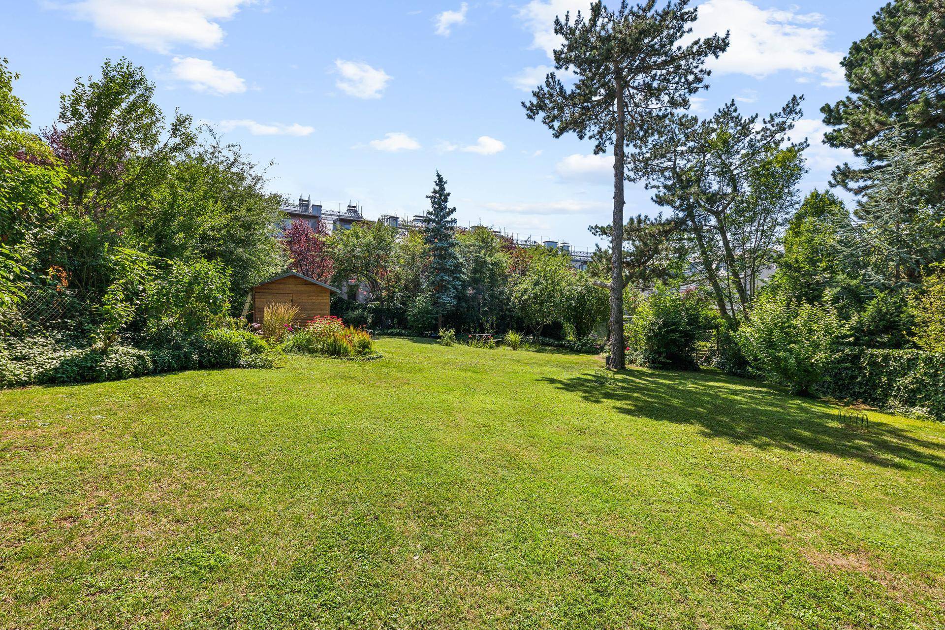 Großer, gepflegter Garten mit weitläufiger Rasenfläche, alten Bäumen und einem kleinen Gartenhaus.