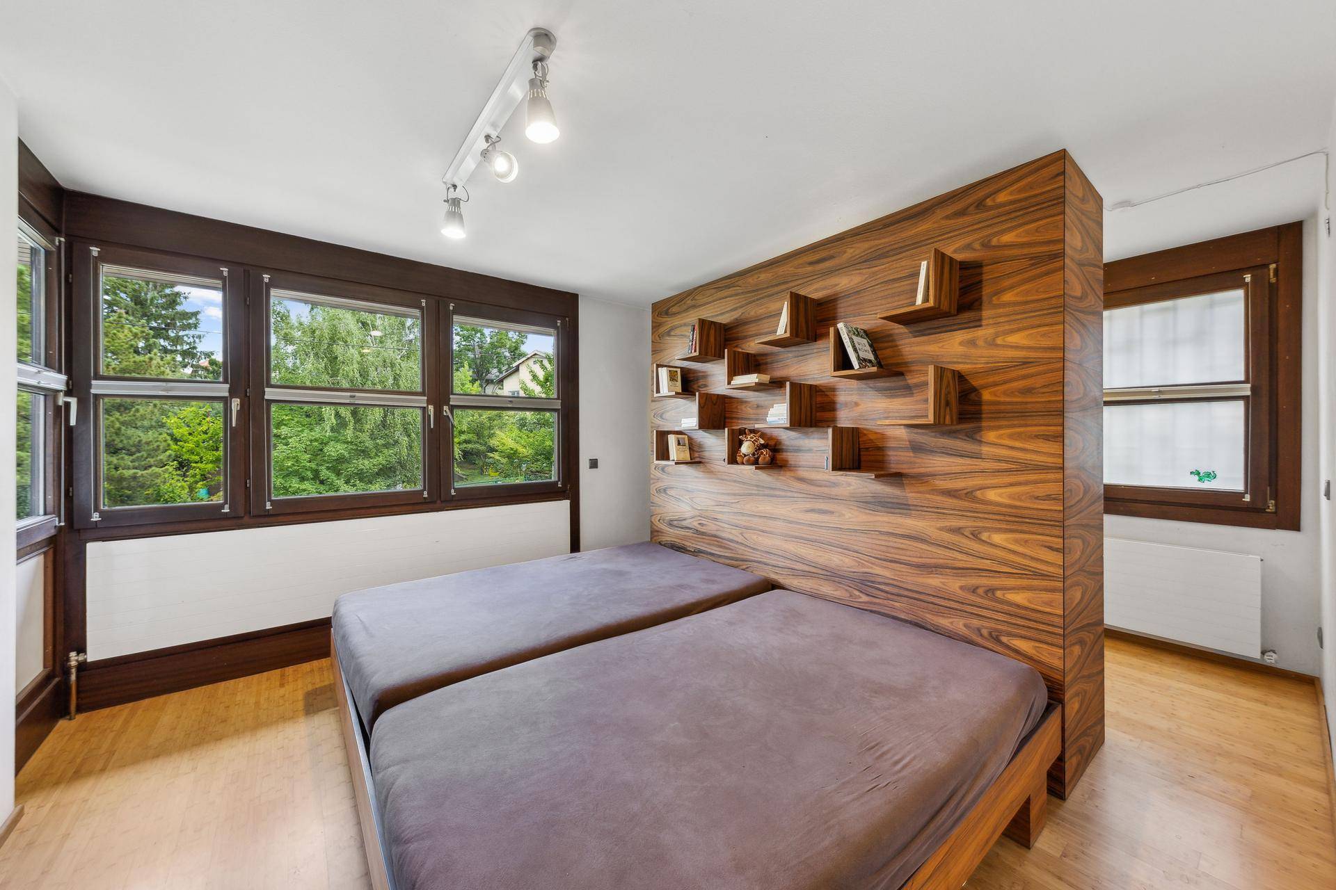 Schlafzimmer mit Holzbett, integriertem Regal und großen Fenstern, die einen schönen Blick ins Grüne bieten.