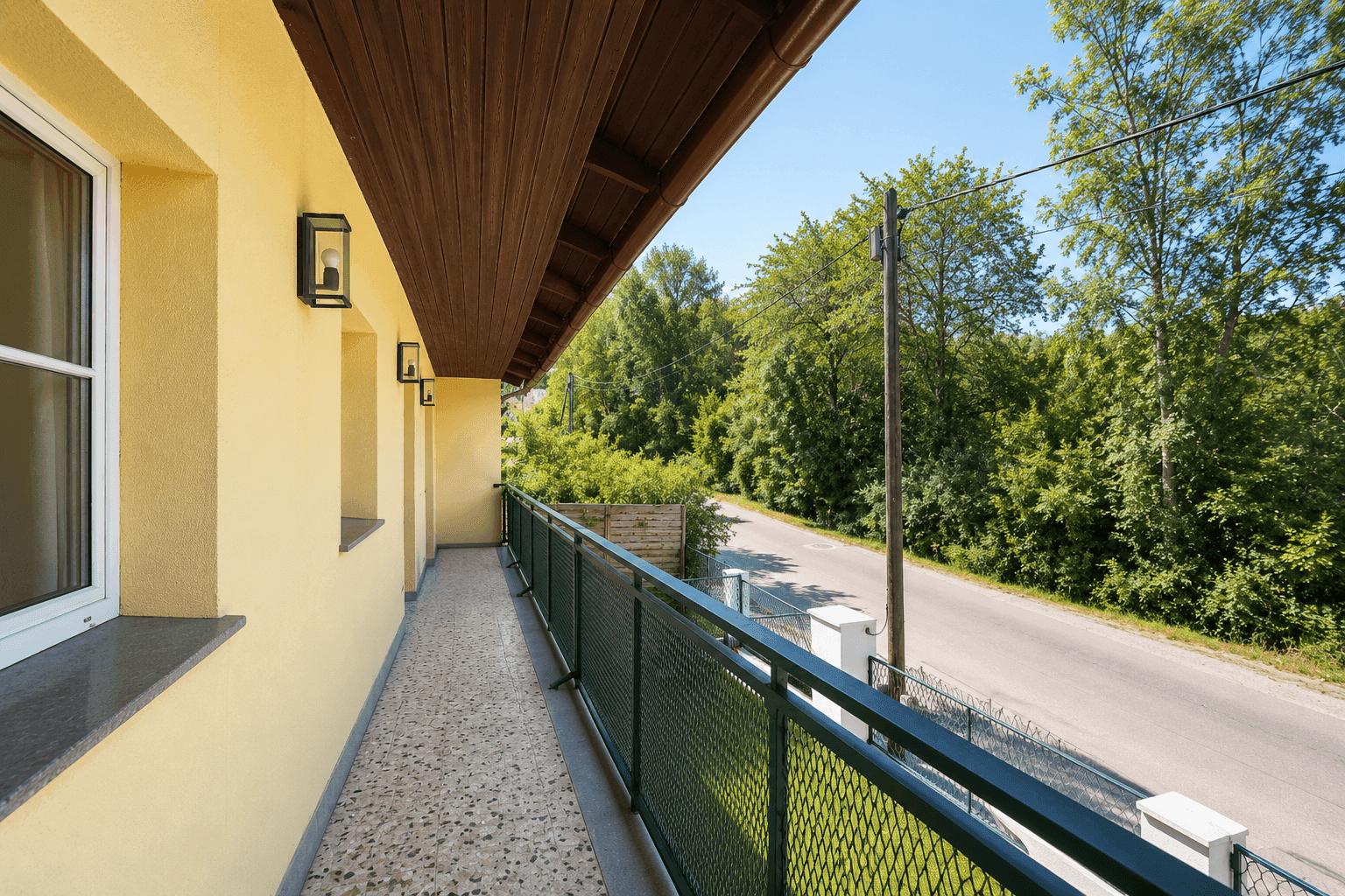 Langer Balkon mit Metallgeländer entlang der Hausfassade und Blick auf die Straße.