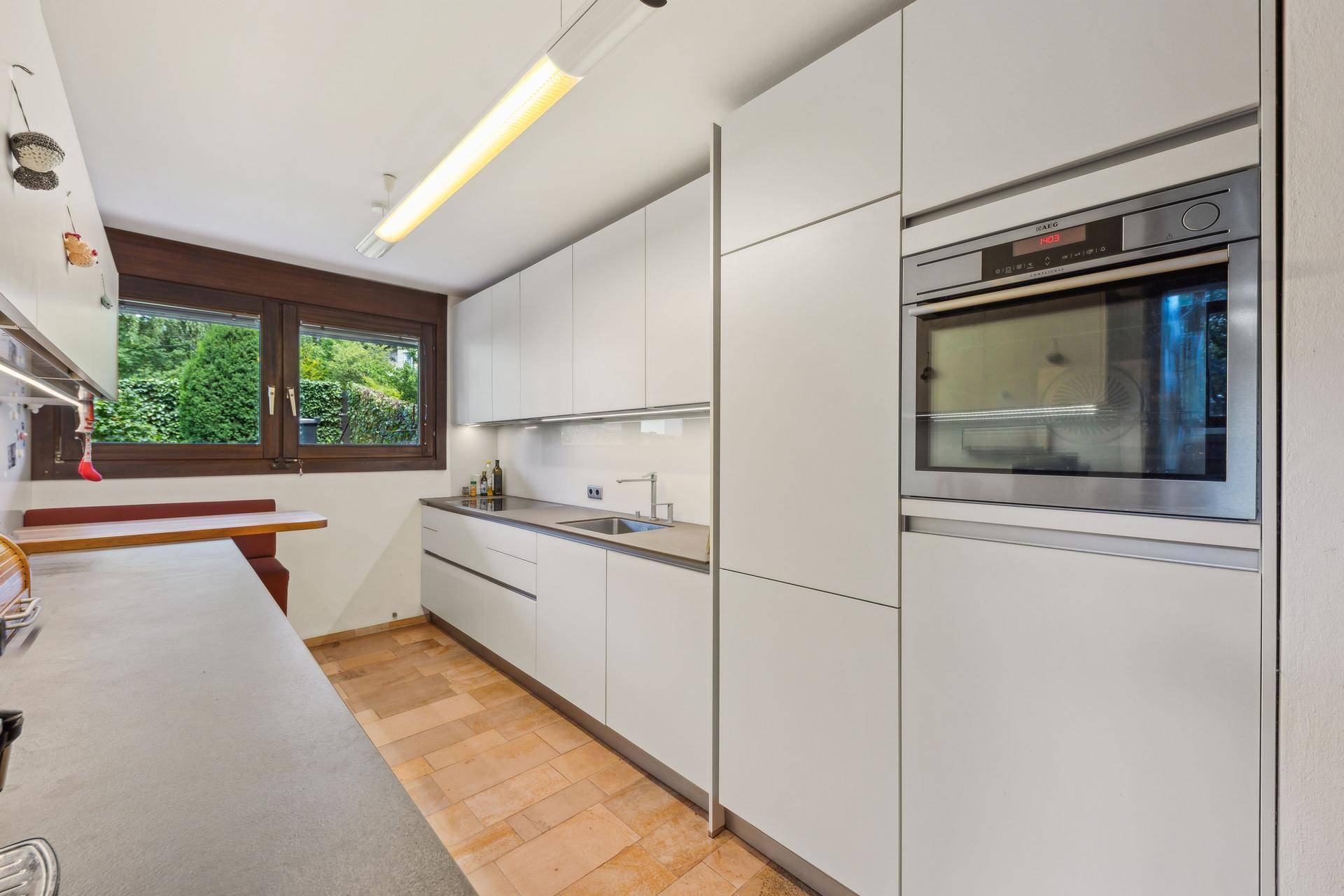 Moderne Küche mit weißen Hochglanzschränken, integrierten Geräten und einem Fenster zum Garten.