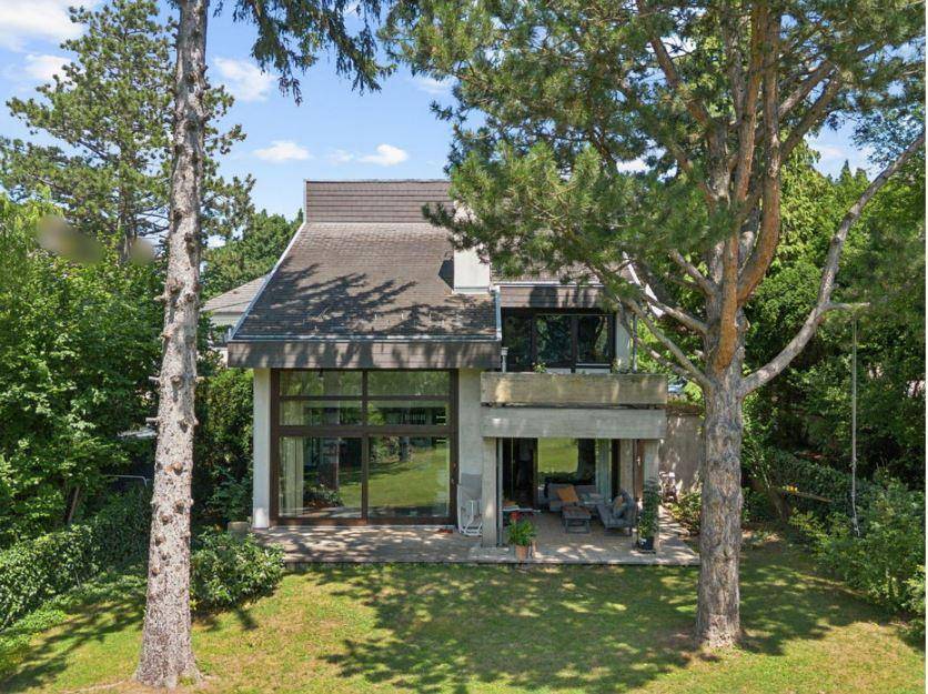 Modernes Einfamilienhaus mit großen Fensterfronten und umgebendem Grün, eingebettet in die Natur.