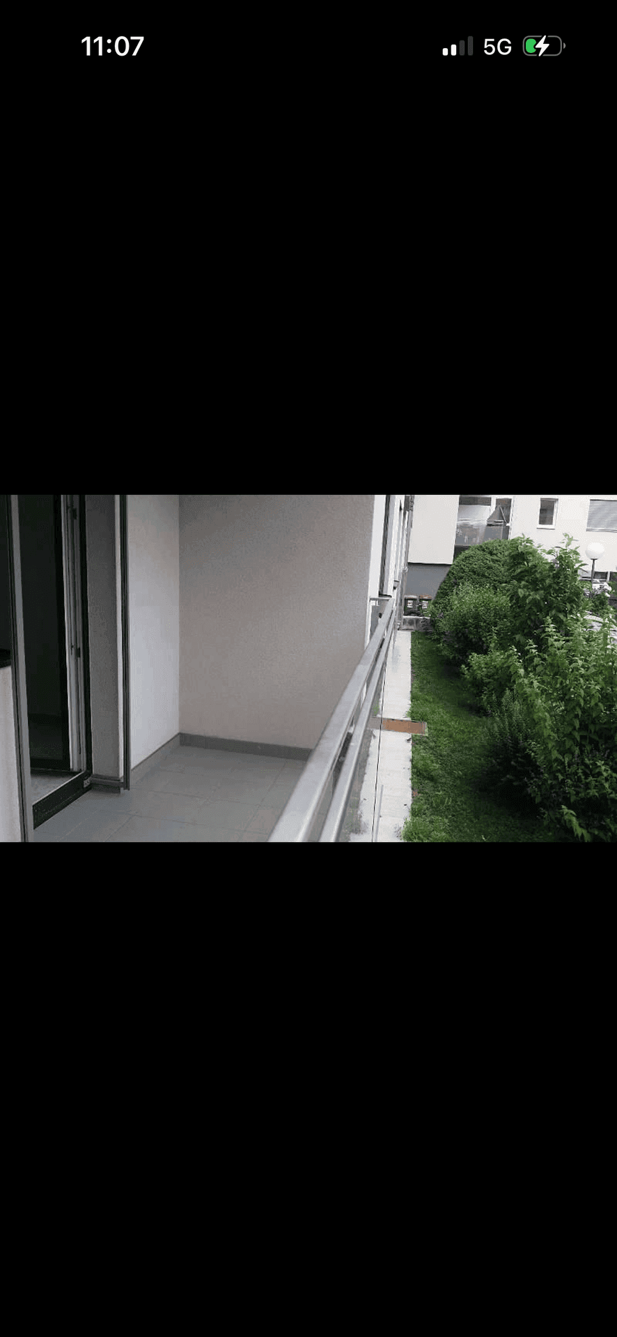 Schmaler Balkon mit Fliesenboden und Blick auf grüne Büsche und angrenzende Gebäude.