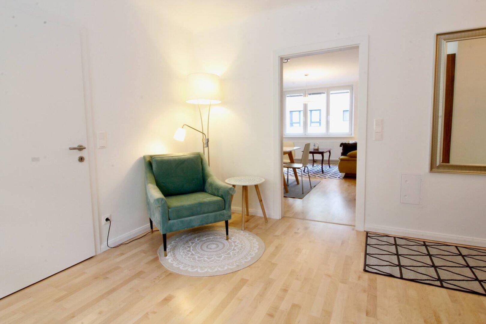 Heller Flur mit grünem Sessel, Stehlampe und Blick in den Wohnbereich.