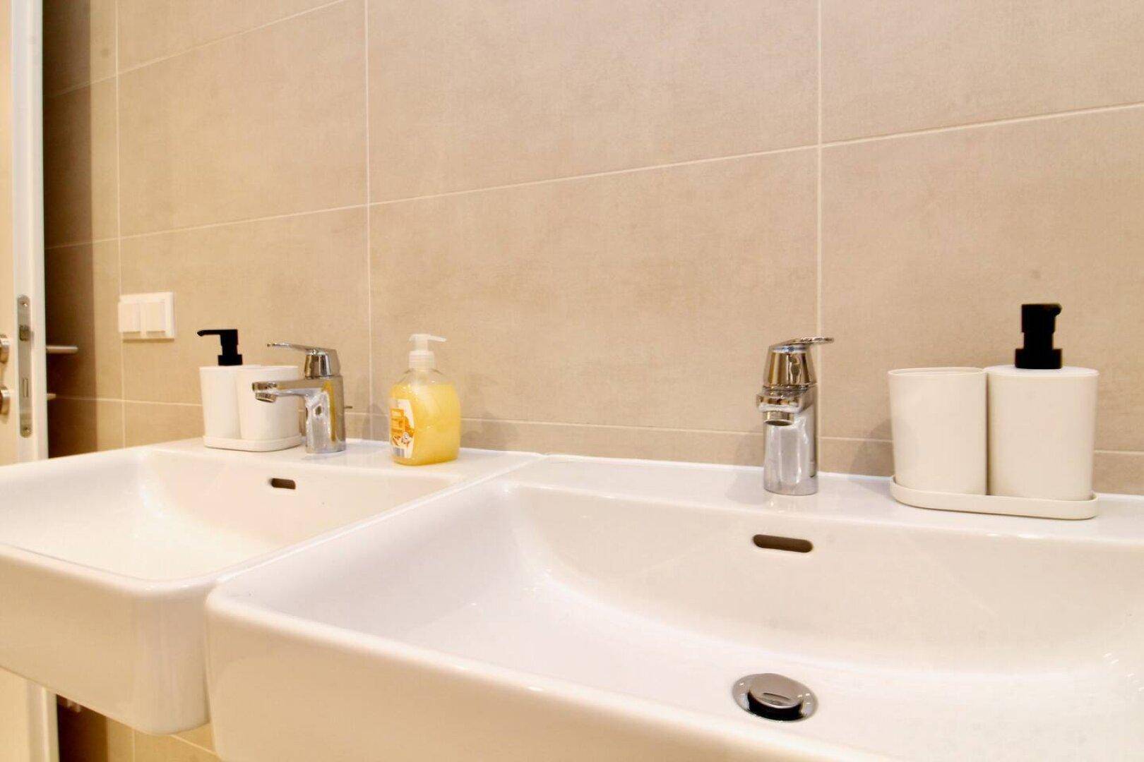 Modernes Badezimmer mit zwei Waschbecken und beigefarbenen Fliesen.