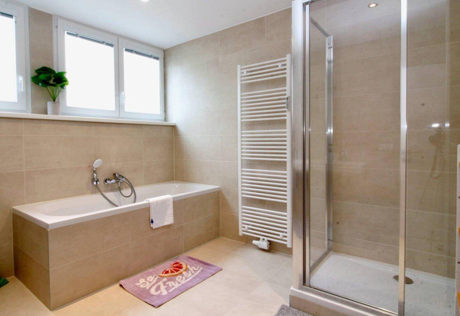 Modernes Badezimmer mit Badewanne, Dusche und beheiztem Handtuchhalter.