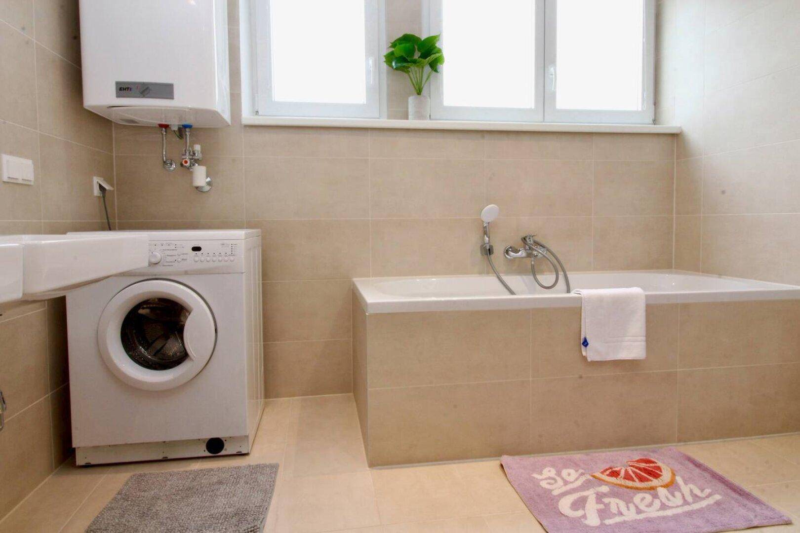 Badezimmer mit Badewanne, Waschmaschine und Fenster für Tageslicht.