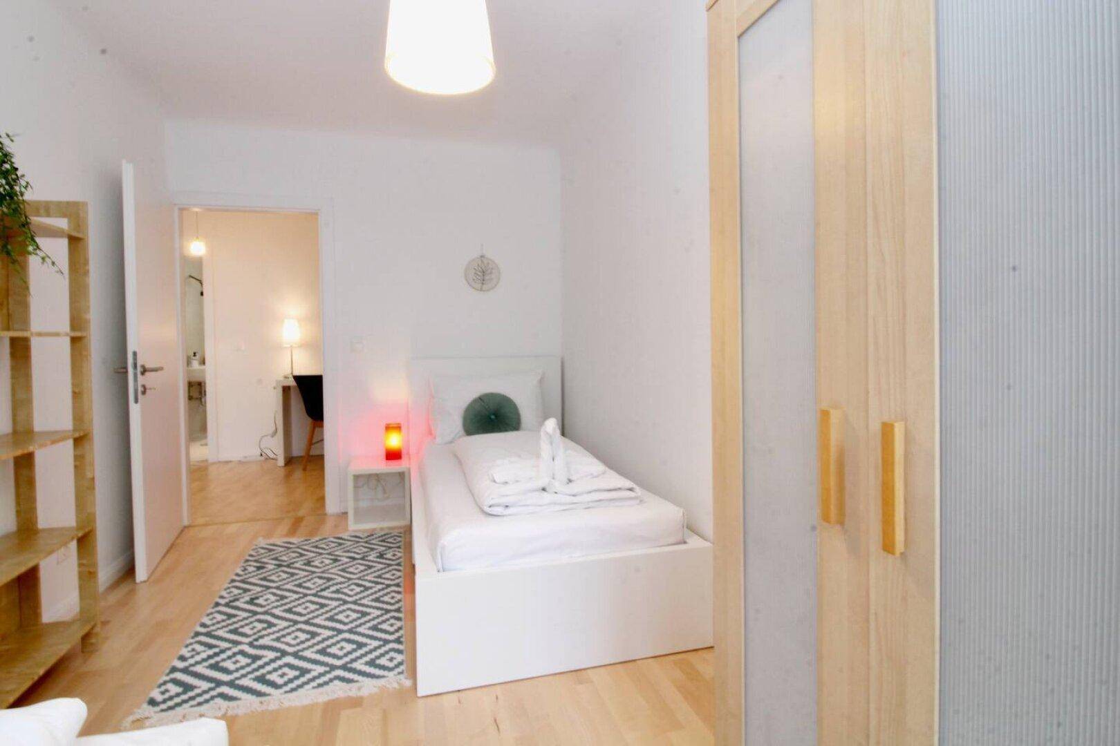 Helles Schlafzimmer mit Einzelbett, Kleiderschrank und Holzboden.