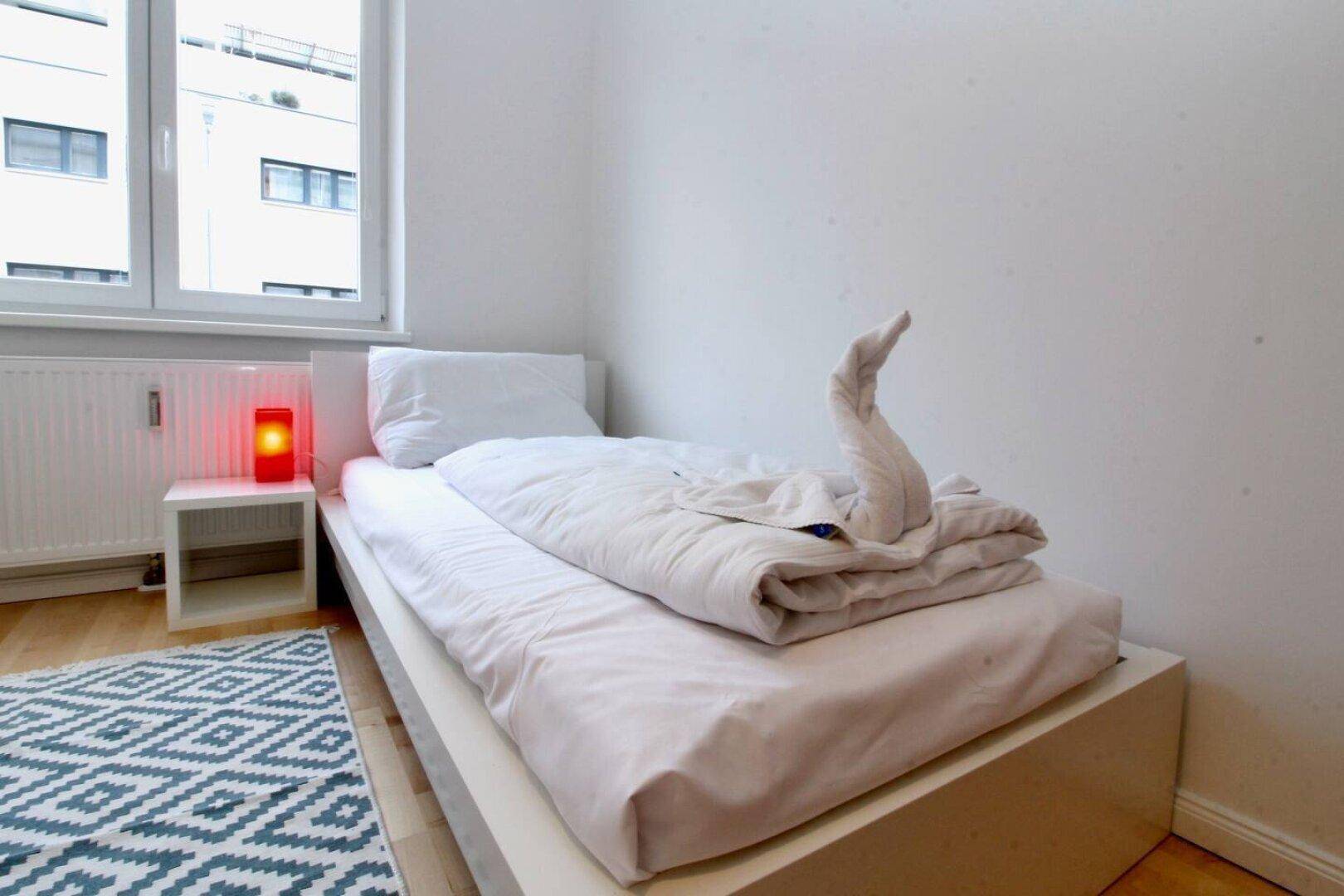 Schlafzimmer mit Einzelbett, Nachttisch und Fenster mit Blick nach draußen.