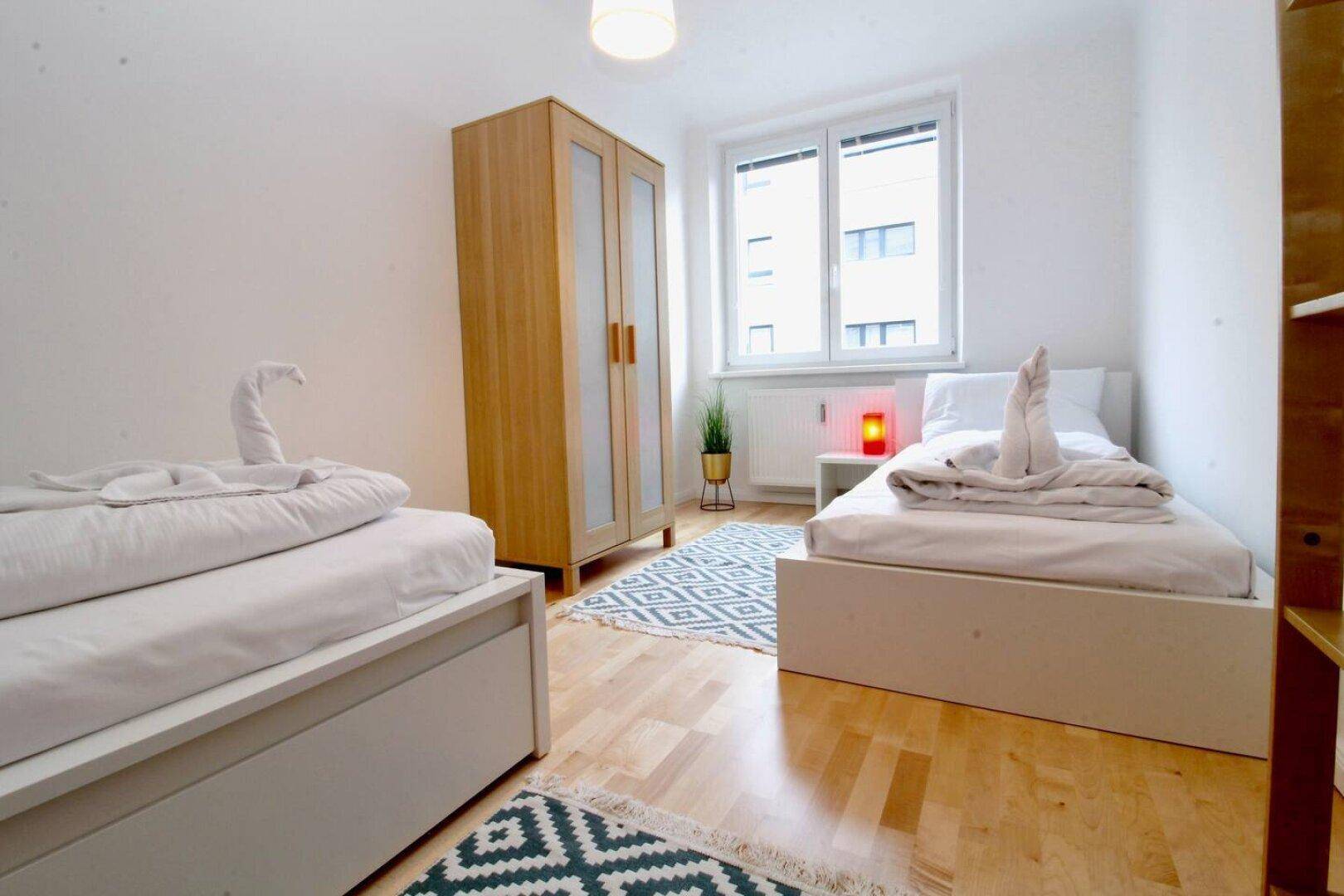 Schlafzimmer mit zwei Einzelbetten, Kleiderschrank und Fenster.