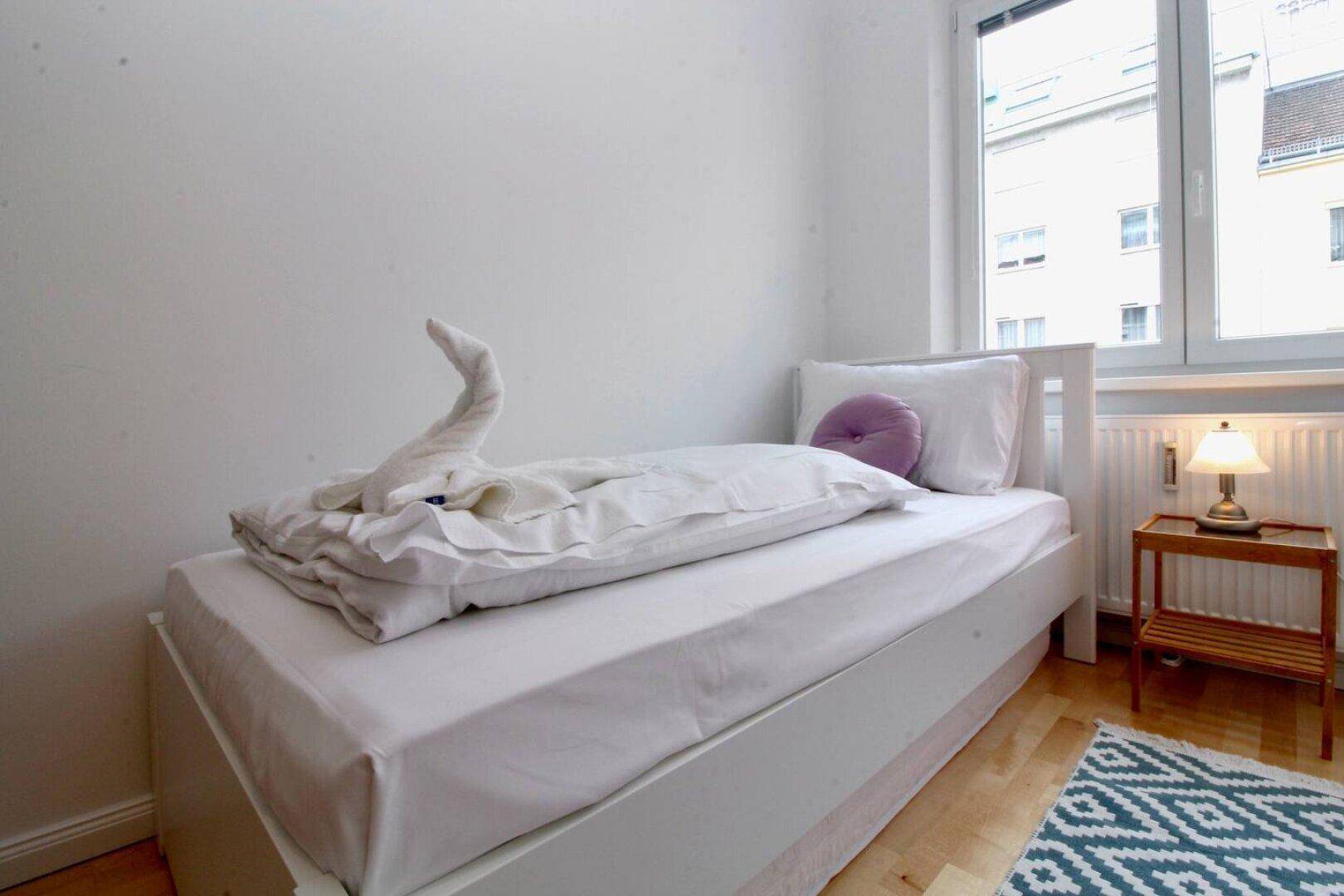 Gemütliches Schlafzimmer mit Einzelbett, Nachttisch und Fenster.