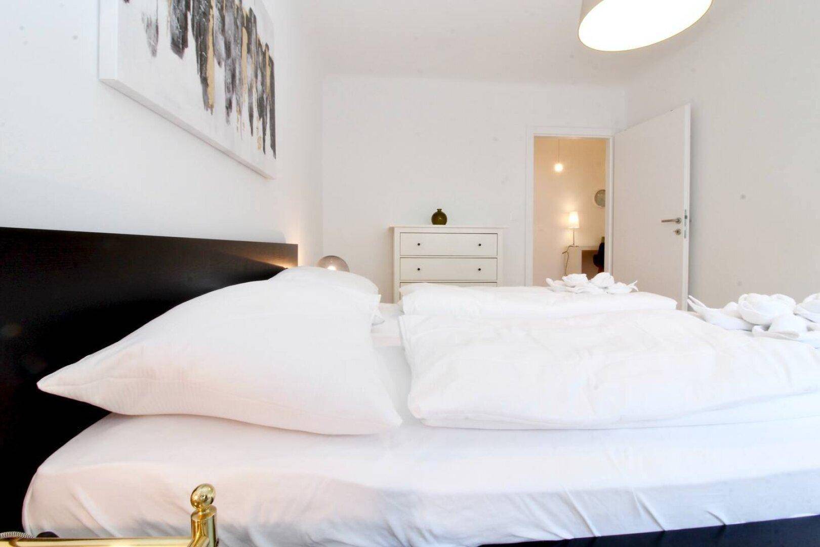 Helles Schlafzimmer mit Doppelbett, Nachttisch und moderner Kunst an der Wand.