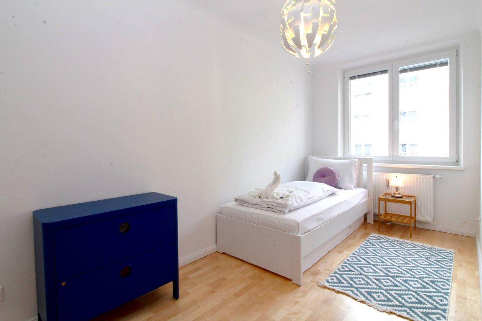 Helles Schlafzimmer mit Einzelbett, blauer Kommode und Holzboden.