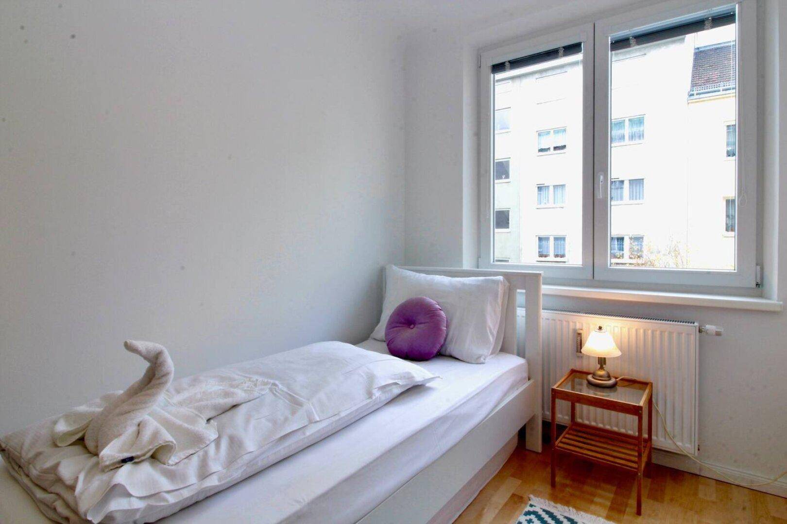 Schlafzimmer mit Einzelbett, Nachttisch und Blick aus dem Fenster.