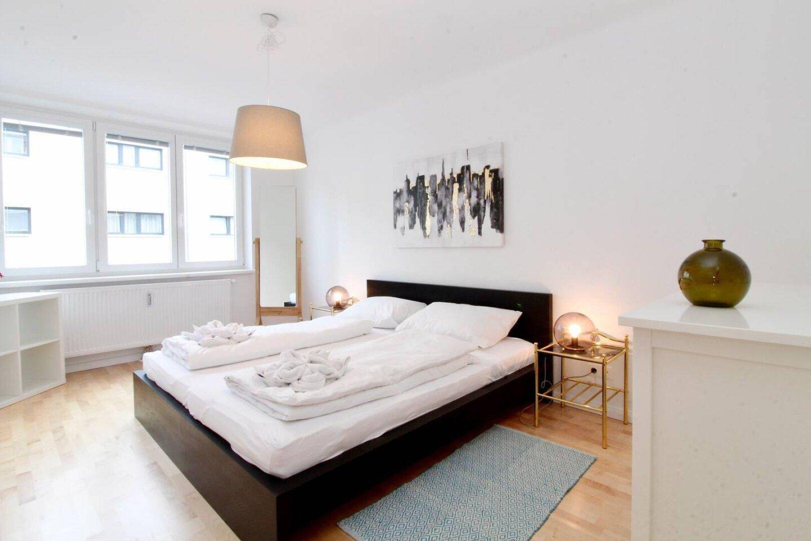 Helles Schlafzimmer mit großem Fenster, Doppelbett und Holzboden.