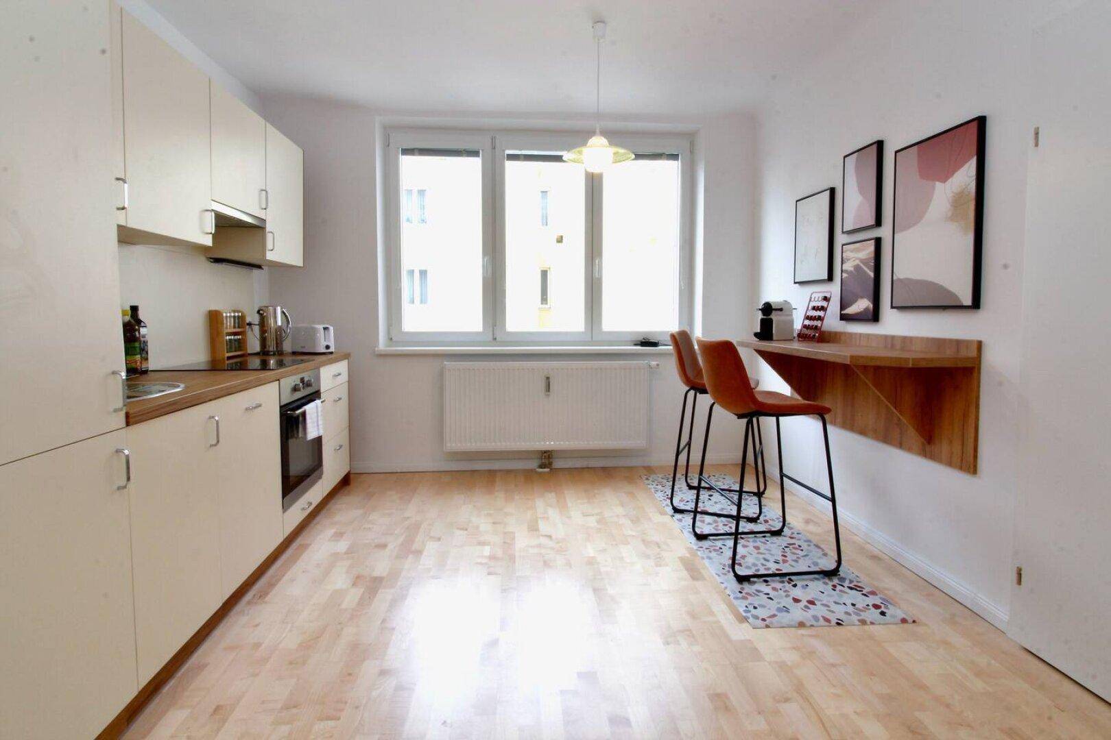 Moderne Küche mit heller Einbauküche, Holzarbeitsplatte und Frühstücksbar am Fenster.