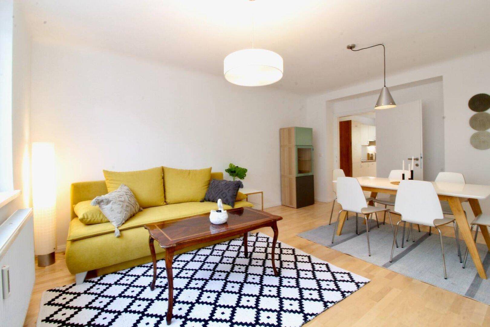 Geräumiger Wohn- und Essbereich mit gelbem Sofa, Esstisch und Holzboden.