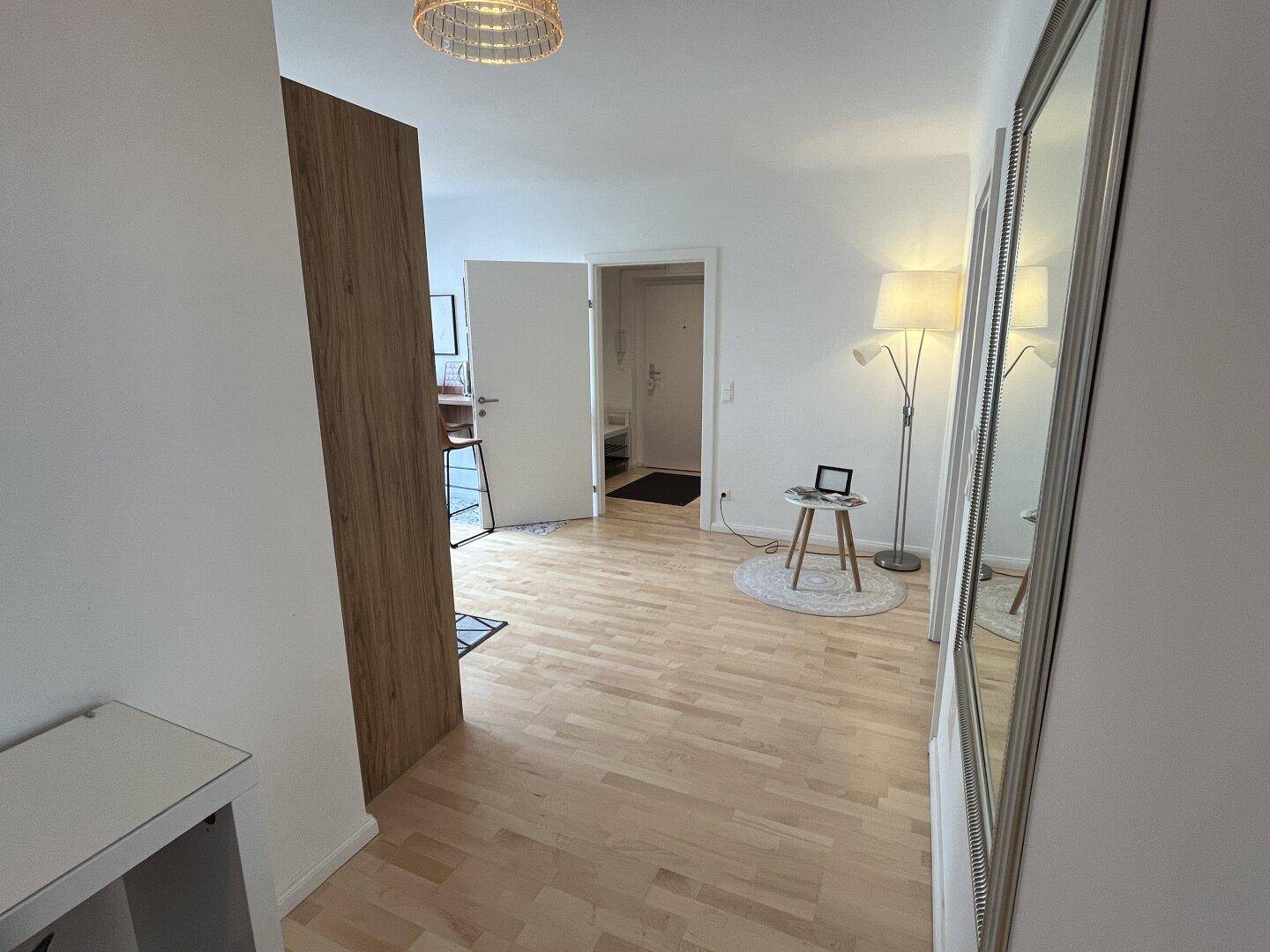Heller Eingangsbereich mit Holzboden, Stehlampe und großem Spiegel.