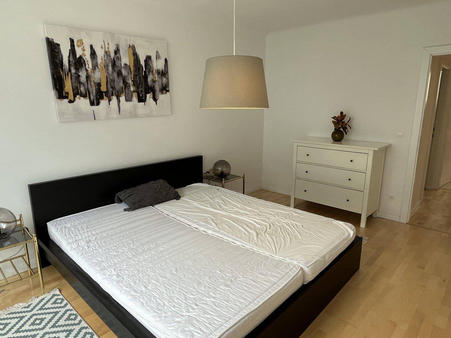 Helles Schlafzimmer mit Doppelbett, Nachttischen und moderner Kunst an der Wand.