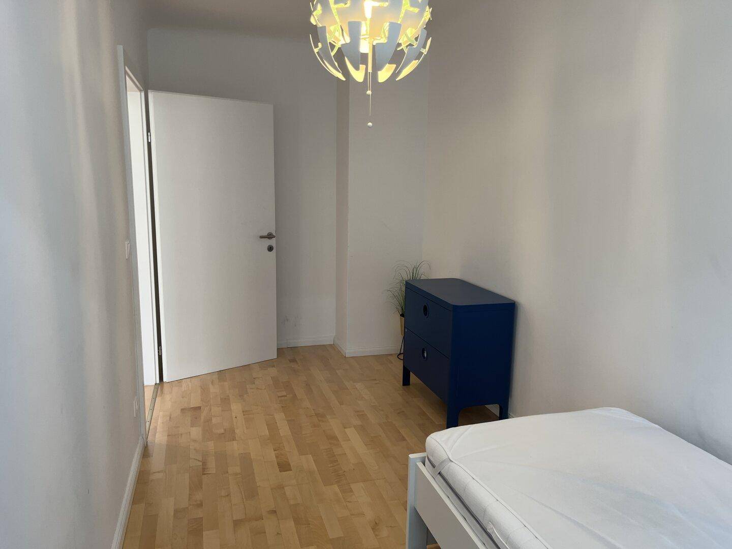 Kleines Schlafzimmer mit Einzelbett, blauer Kommode und Holzboden.