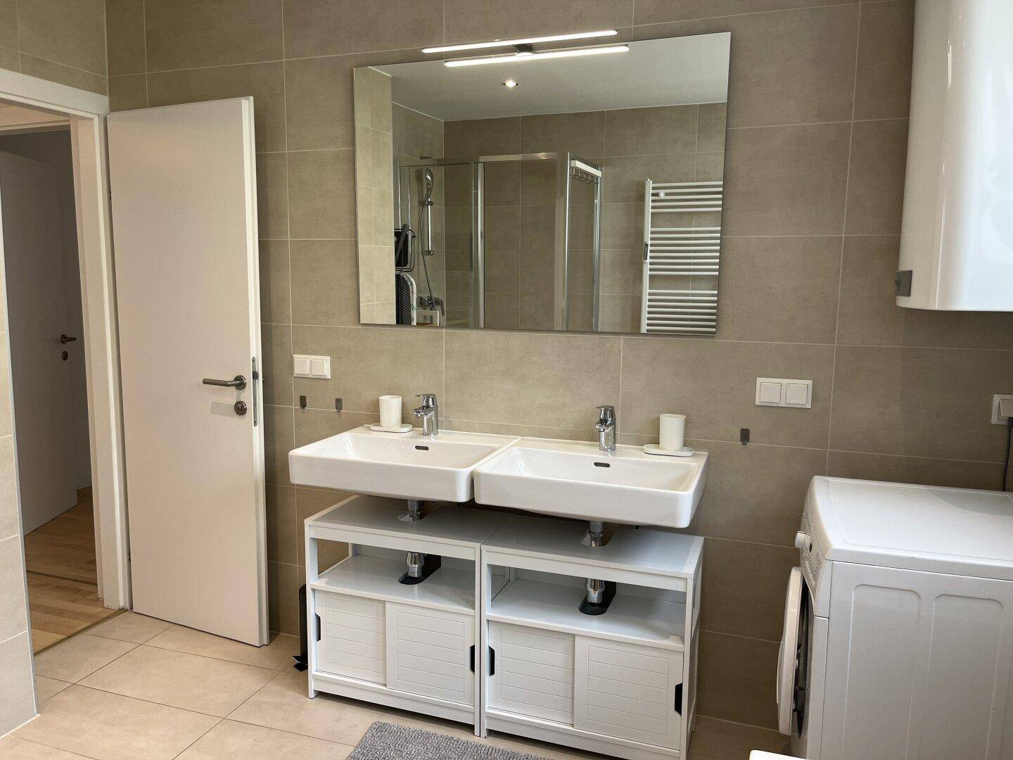 Geräumiges Badezimmer mit Doppelwaschbecken, Dusche und Waschmaschine.