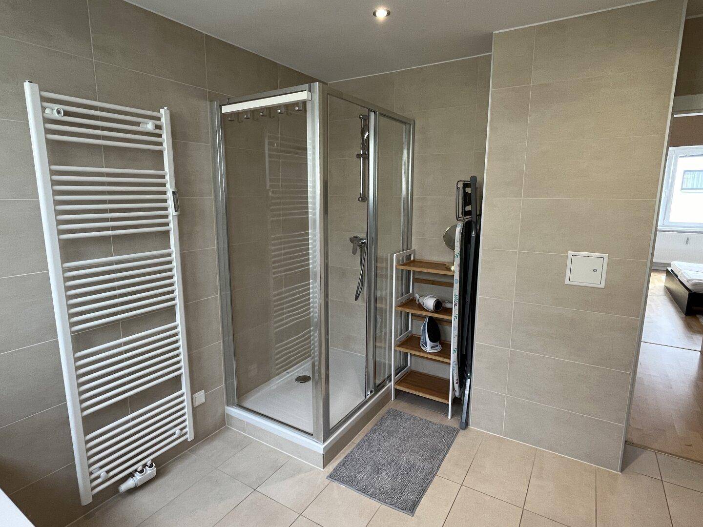 Modernes Badezimmer mit Duschkabine, Handtuchheizkörper und hellen Fliesen.