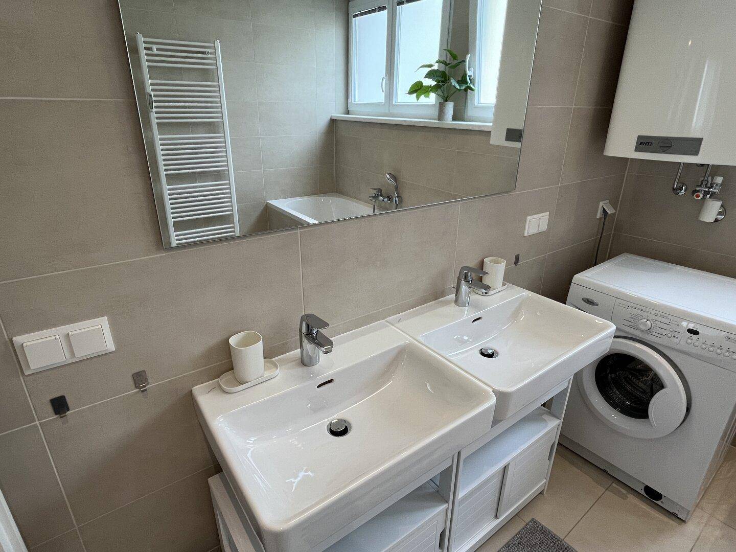 Funktionales Badezimmer mit Doppelwaschbecken, großem Spiegel und Waschmaschine.