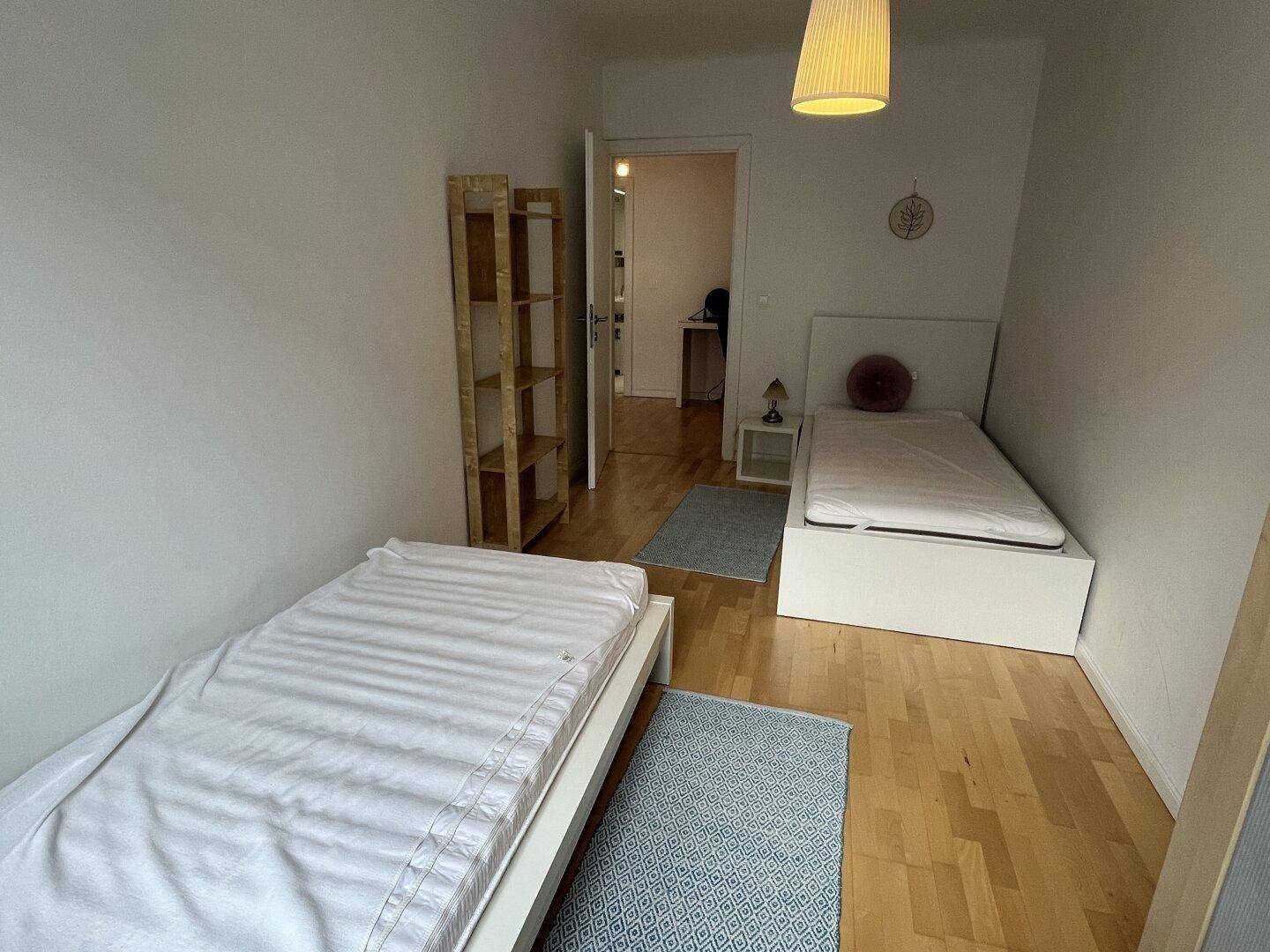 Gemütliches Schlafzimmer mit zwei Einzelbetten, Holzfußboden und offenem Regal.
