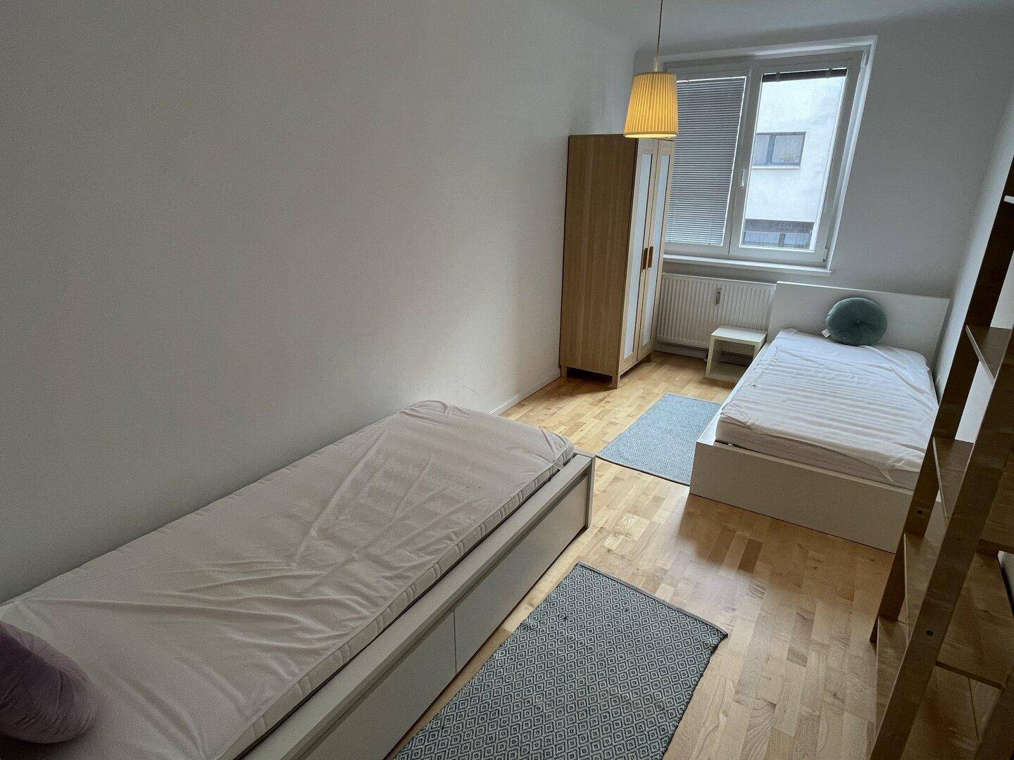 Helles Schlafzimmer mit zwei Einzelbetten, Kleiderschrank und Fenster mit Jalousien.