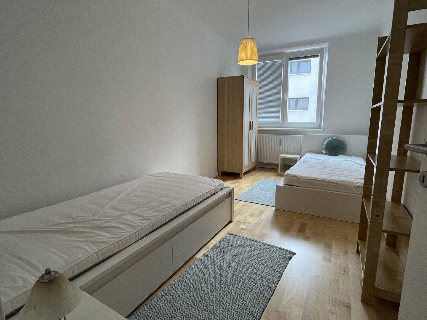 Freundliches Schlafzimmer mit Holzfußboden, zwei Betten und einem Kleiderschrank.
