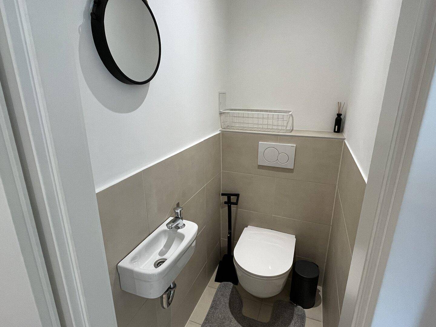 Kleines Gäste-WC mit Wand-WC, Handwaschbecken und modernen Fliesen.