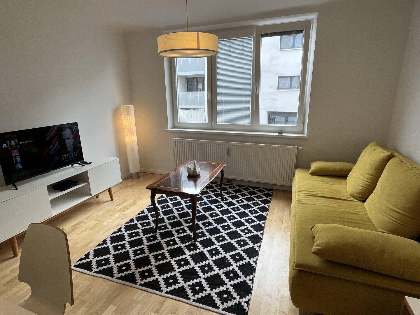 Gemütliches Wohnzimmer mit gelbem Sofa, Couchtisch und Fernseher.