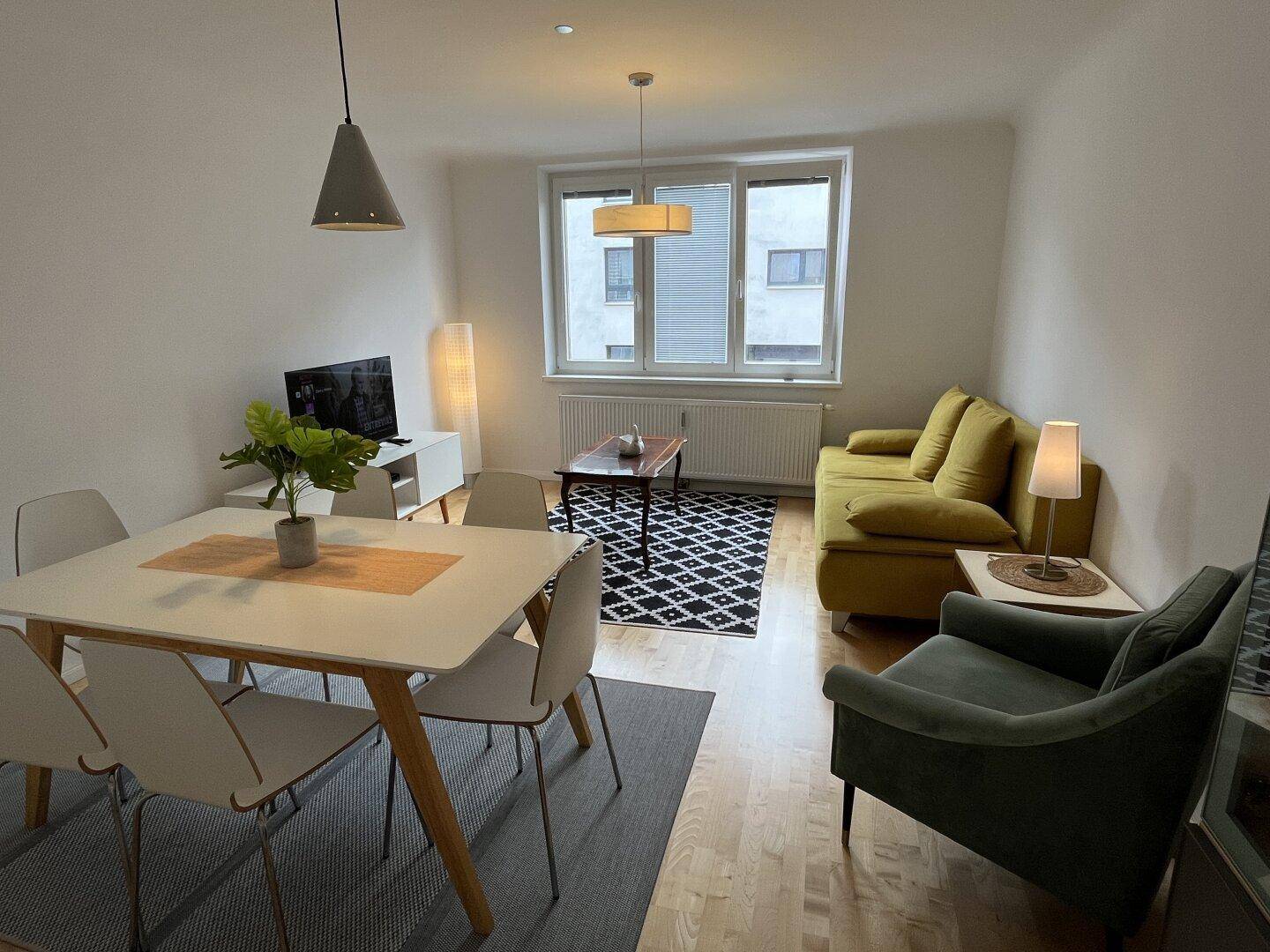 Kombinierter Wohn- und Essbereich mit gelbem Sofa, Esstisch und Blick nach draußen.