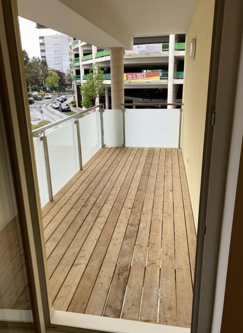 Geräumiger Balkon mit Holzfußboden und Glasgeländer, bietet einen Blick auf die städtische Umgebung.