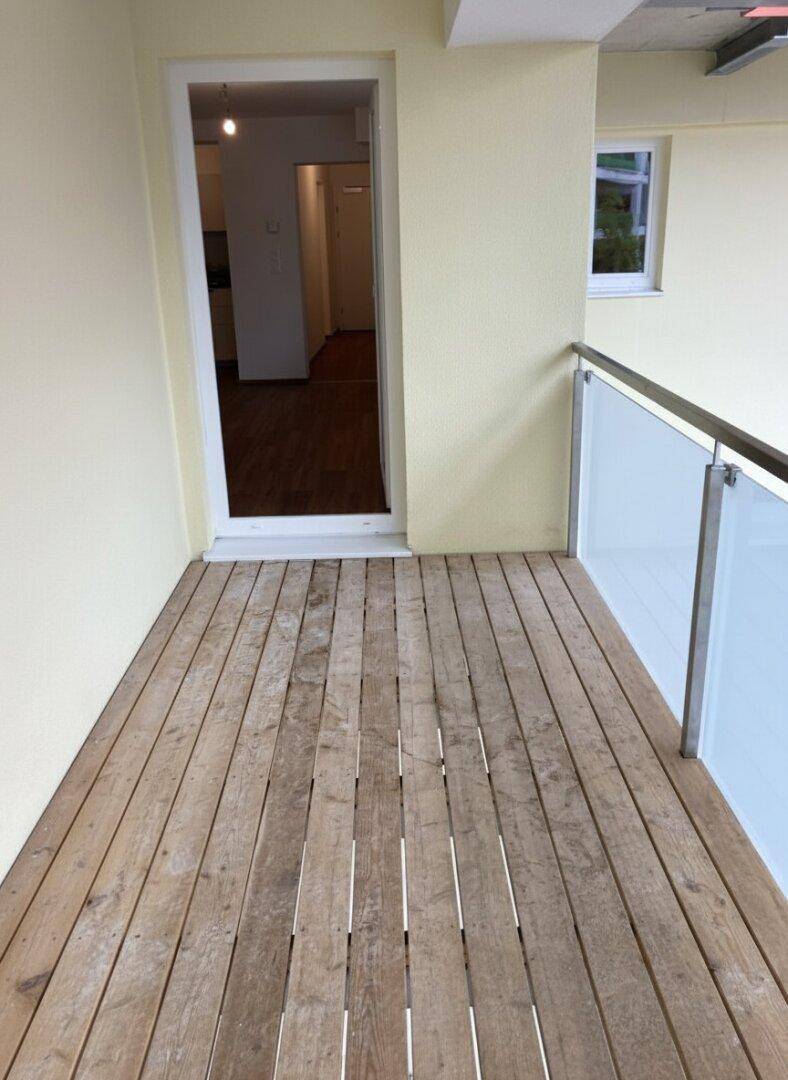 Heller Balkon mit Holzfußboden und Zugang zum Innenbereich der Wohnung.