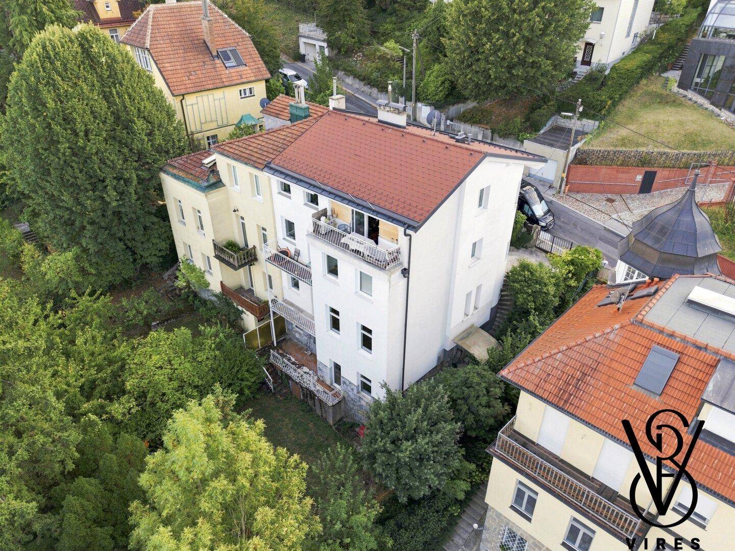Luftaufnahme eines Wohnhauses mit rotem Dach, Balkonen und grüner Umgebung.