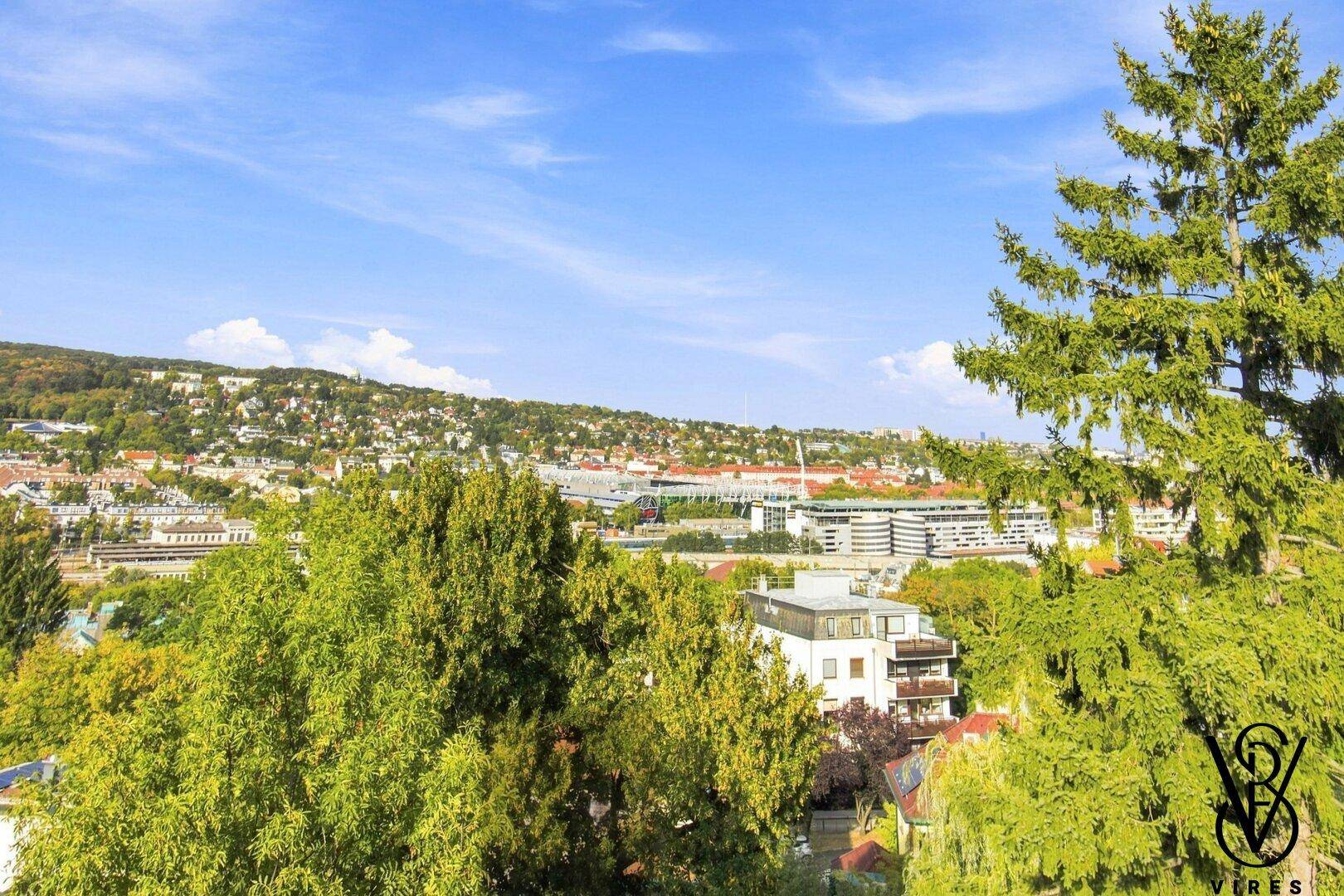 Weitläufiger Blick über eine grüne Hügellandschaft mit städtischer Bebauung im Hintergrund.