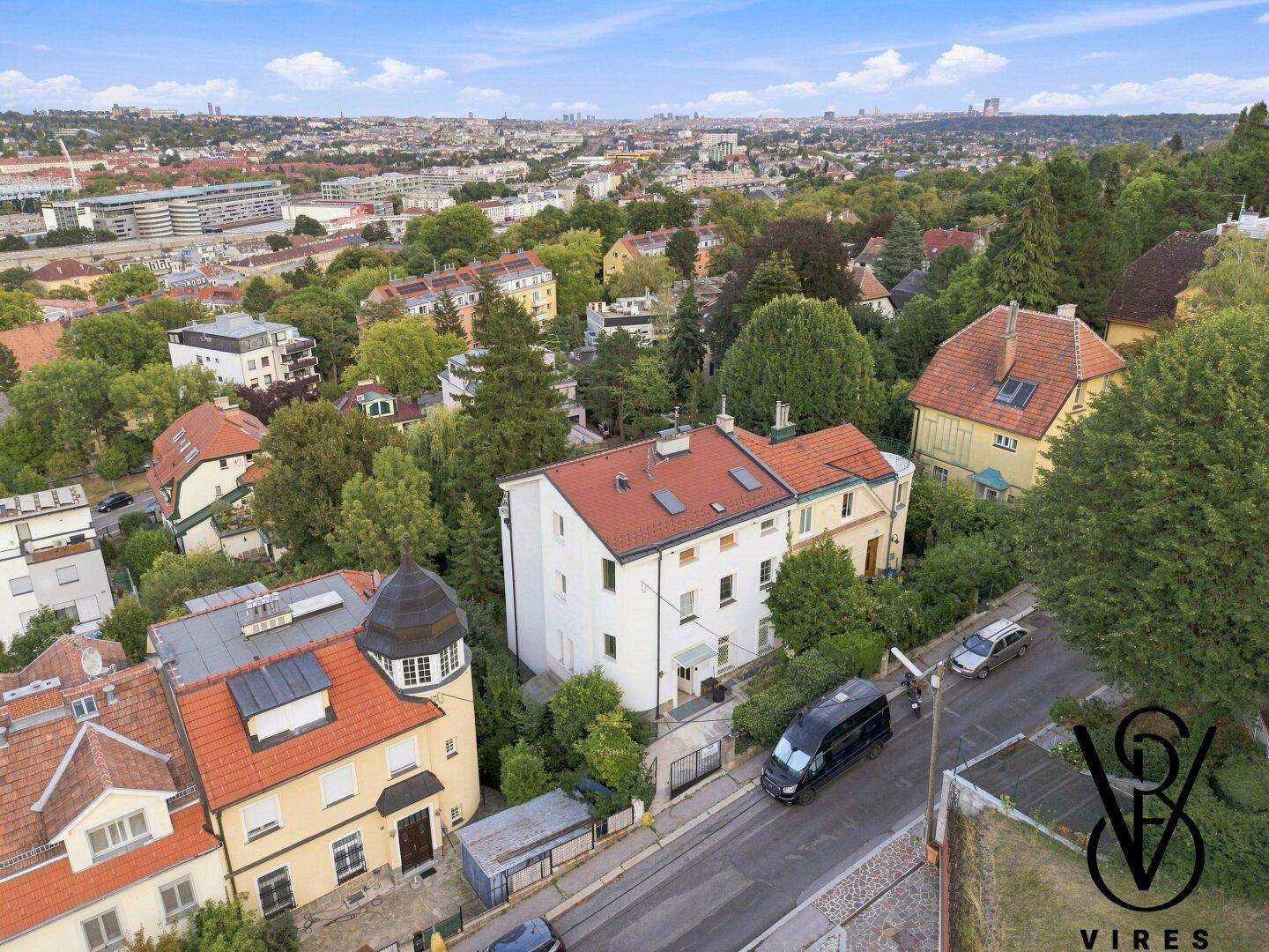 Vogelperspektive eines Wohngebäudes mit rotem Dach, umgeben von Bäumen und weiteren Häusern.