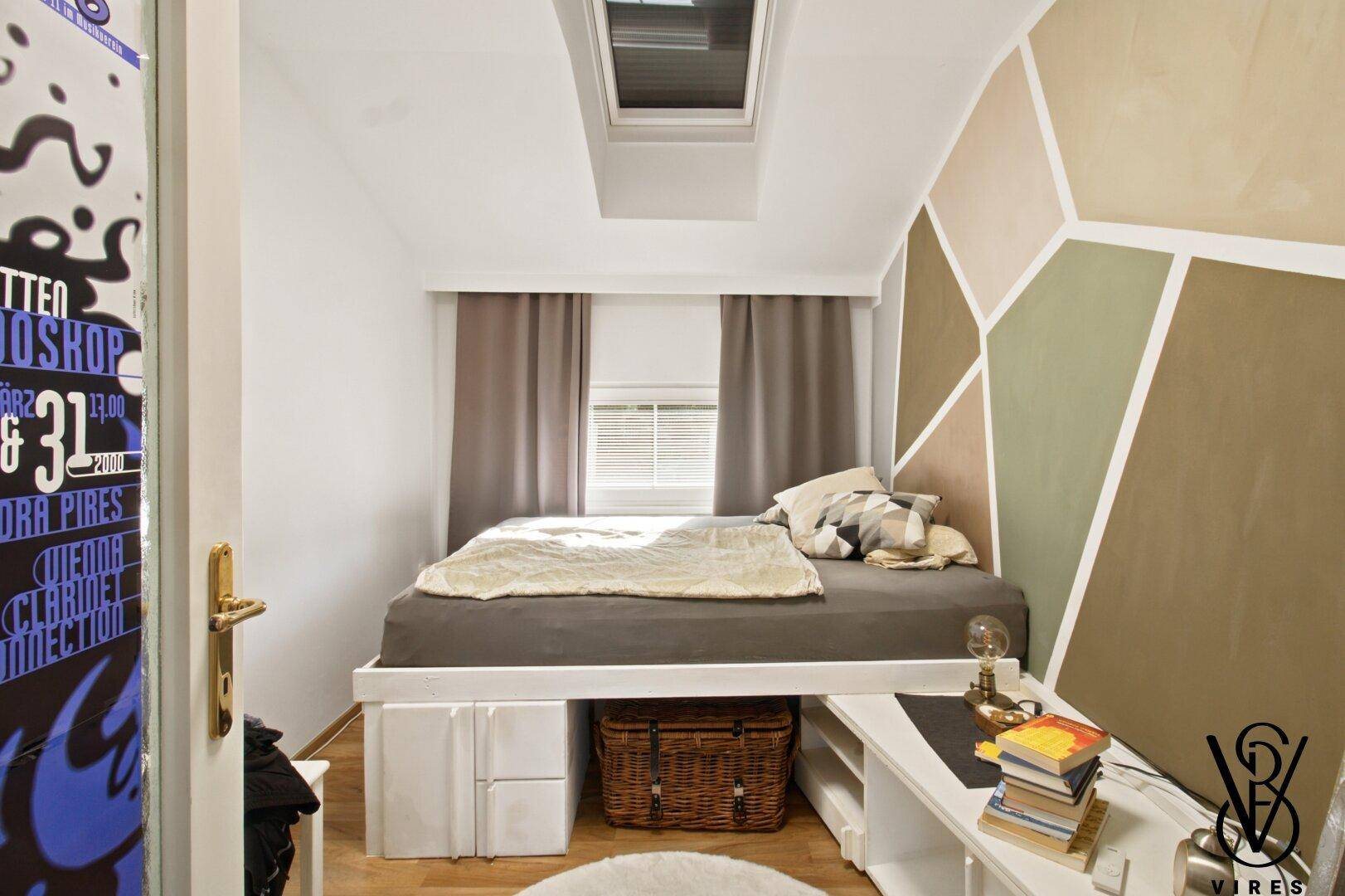 Schlafzimmer mit Bett, Schreibtisch und einem Dachfenster, das viel Licht hereinlässt.