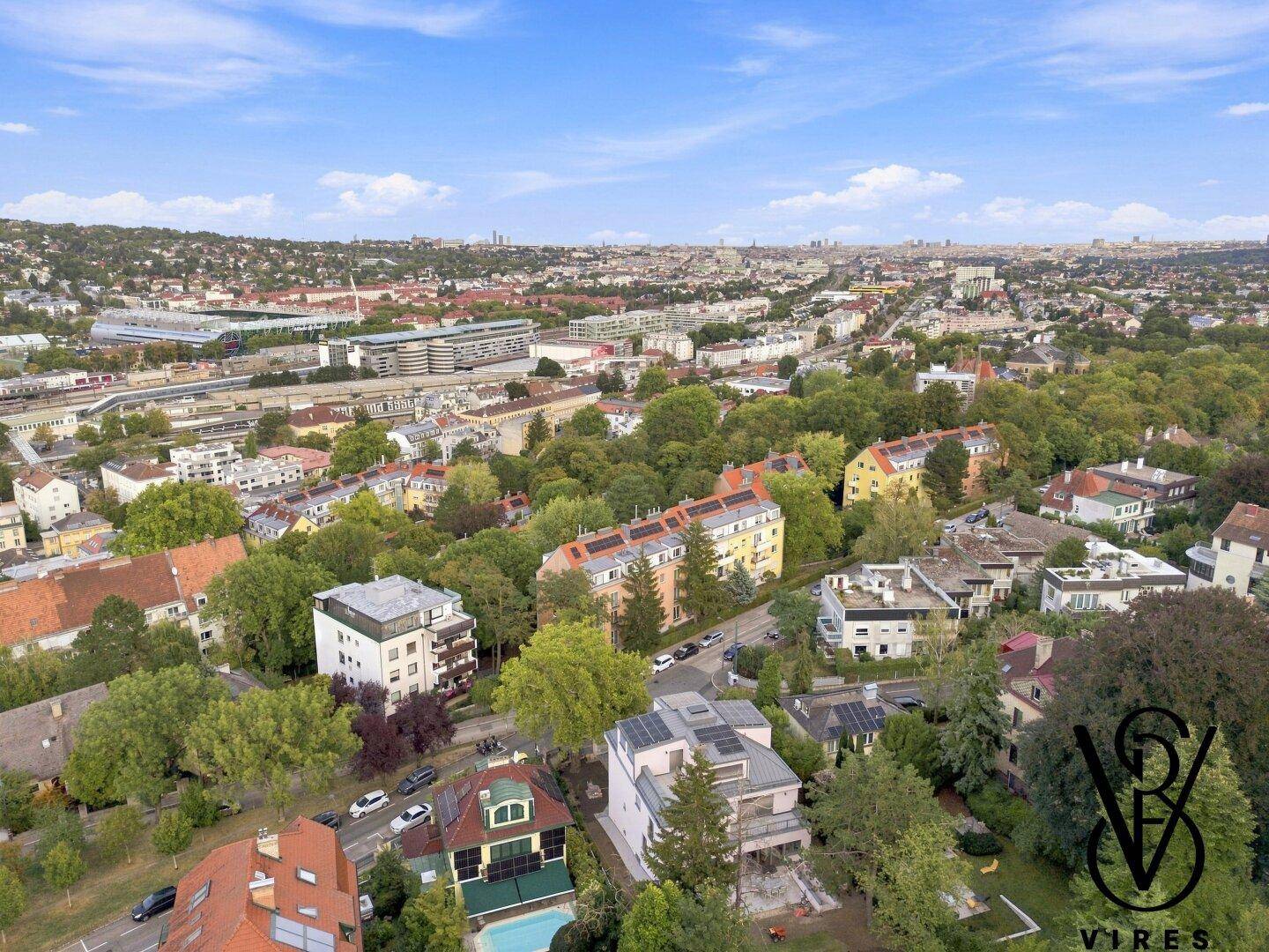 Panoramablick aus der Vogelperspektive auf eine weitläufige Stadtlandschaft mit vielen Gebäuden und Grünflächen.