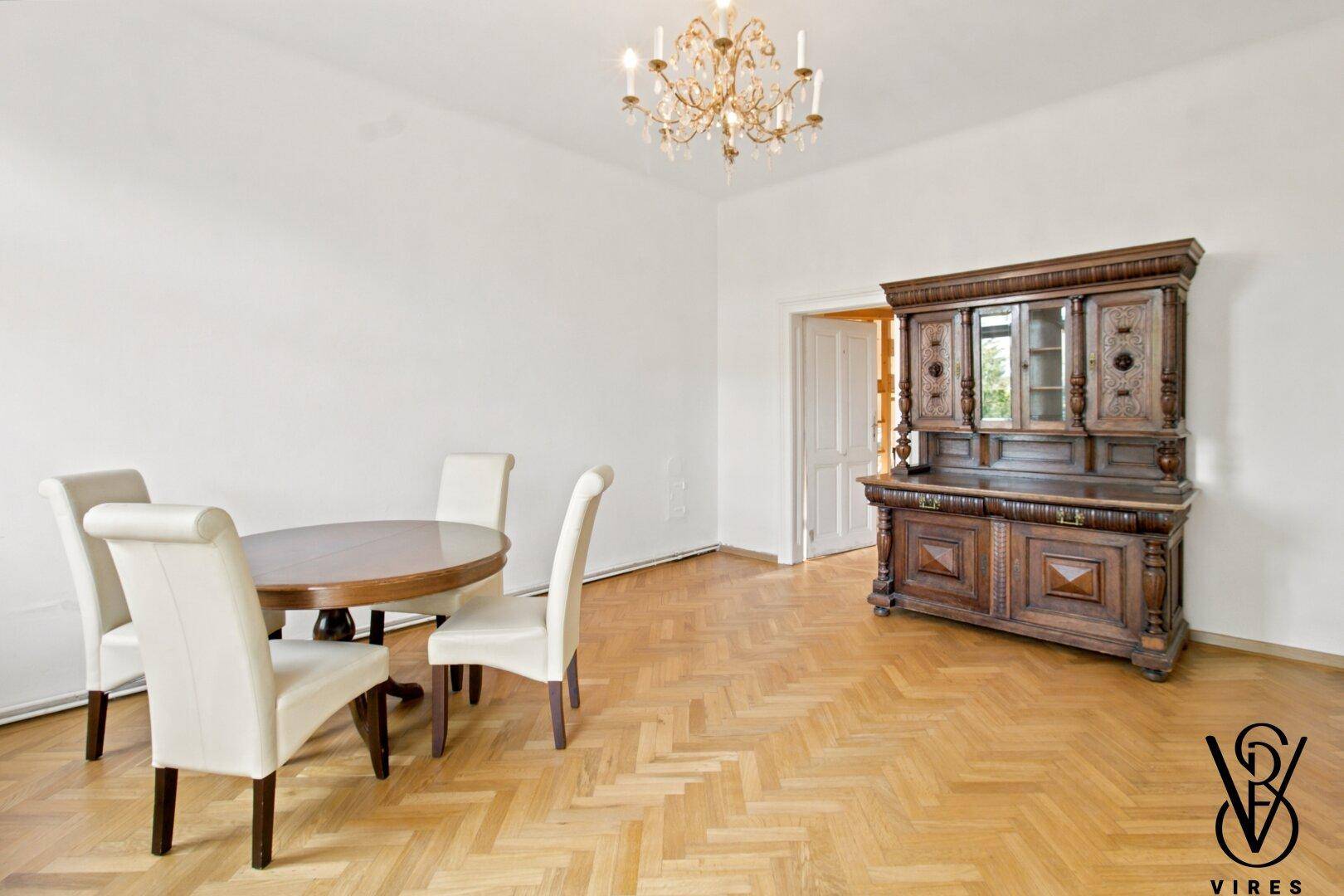 Esszimmer mit Fischgrätparkett, Kronleuchter und einem antiken Holzschrank.