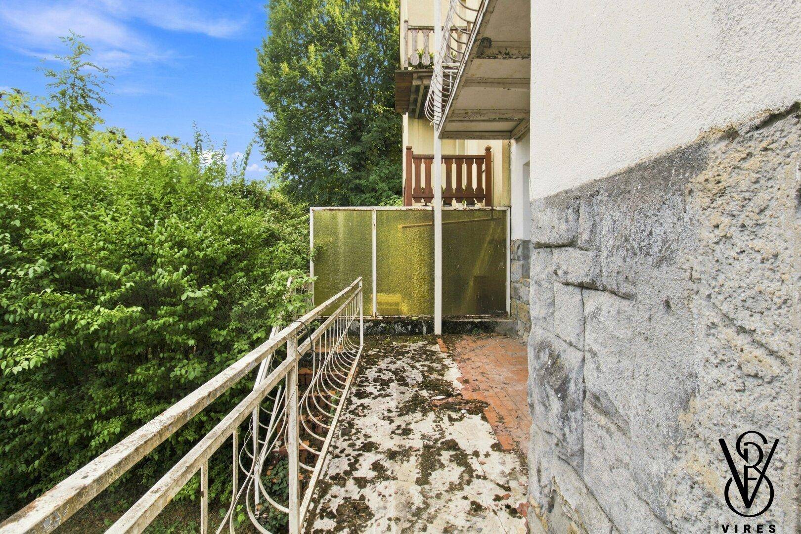 Terrasse mit Steinmauer und Metallgeländer, umgeben von viel Grün.