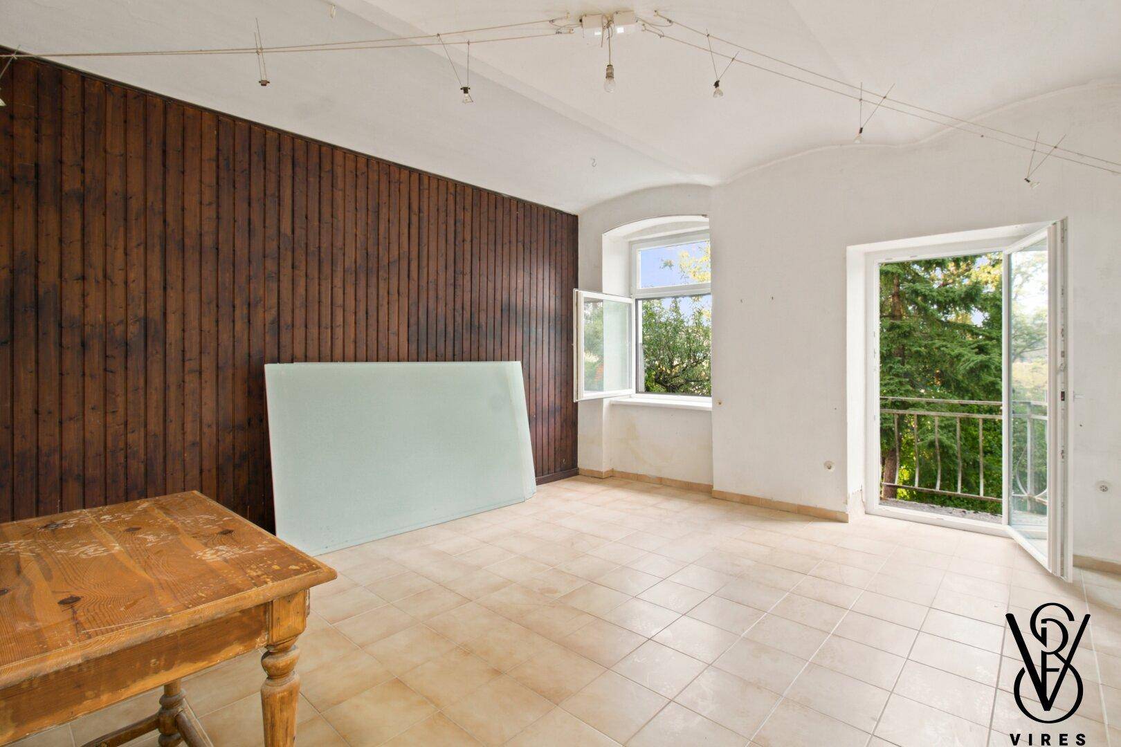 Geräumiges Wohnzimmer mit Holzvertäfelung, Fliesenboden und Balkonzugang.