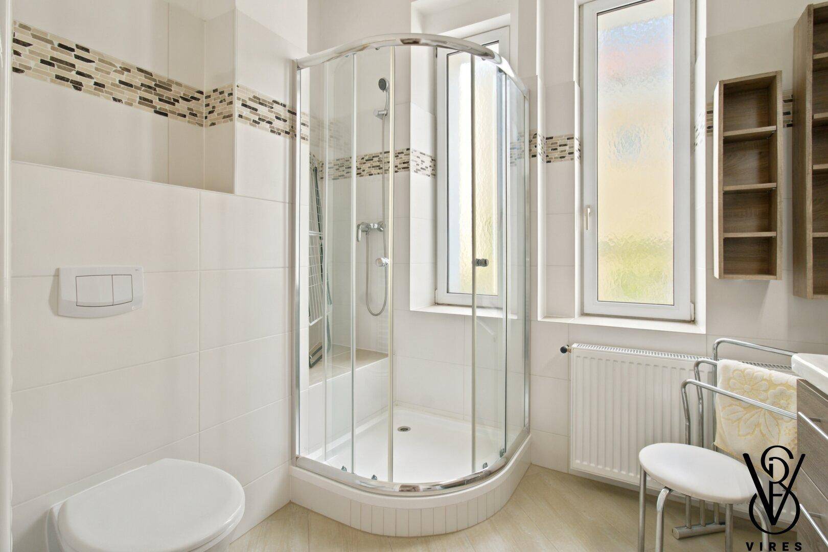 Badezimmer mit Duschkabine, Wand-WC und Fenster.