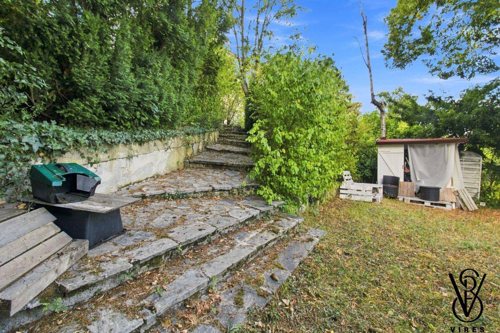Steintreppe im Garten, umgeben von üppigem Grün und Bäumen.