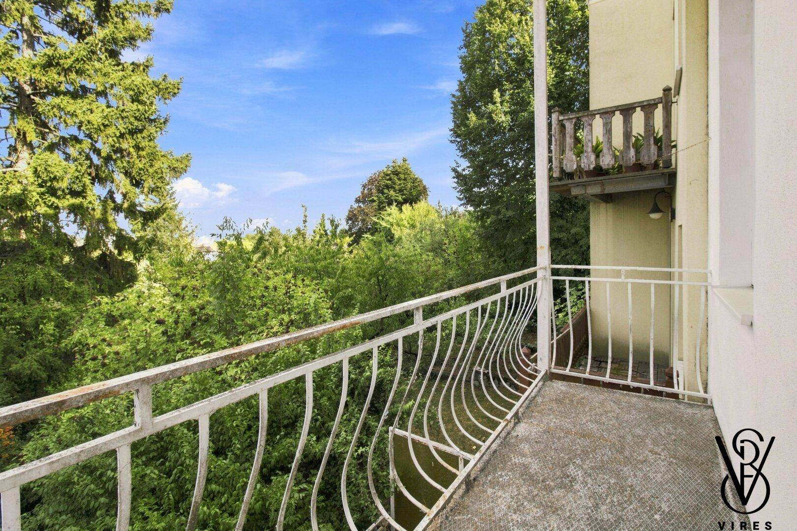 Balkon mit schmiedeeisernem Geländer und üppigem Grünblick.