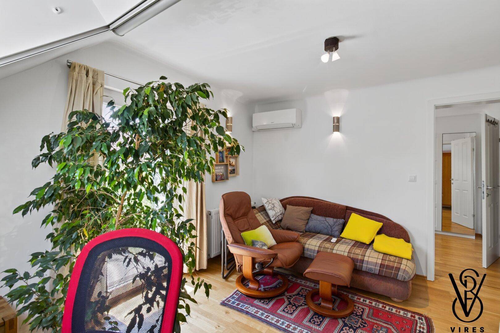 Gemütlicher Wohnbereich mit bequemer Chaiselongue, Zimmerpflanze und Klimaanlage unter dem Dach.