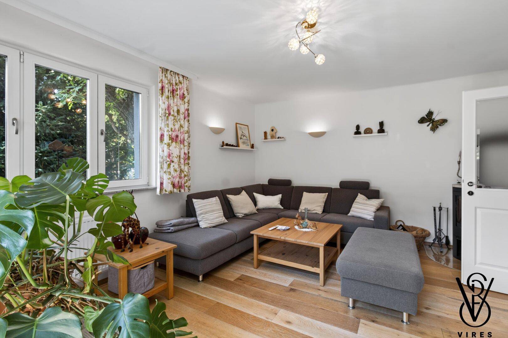 Geräumiges Wohnzimmer mit Ecksofa, Holzofen und hellem Holzboden, ideal zum Entspannen.