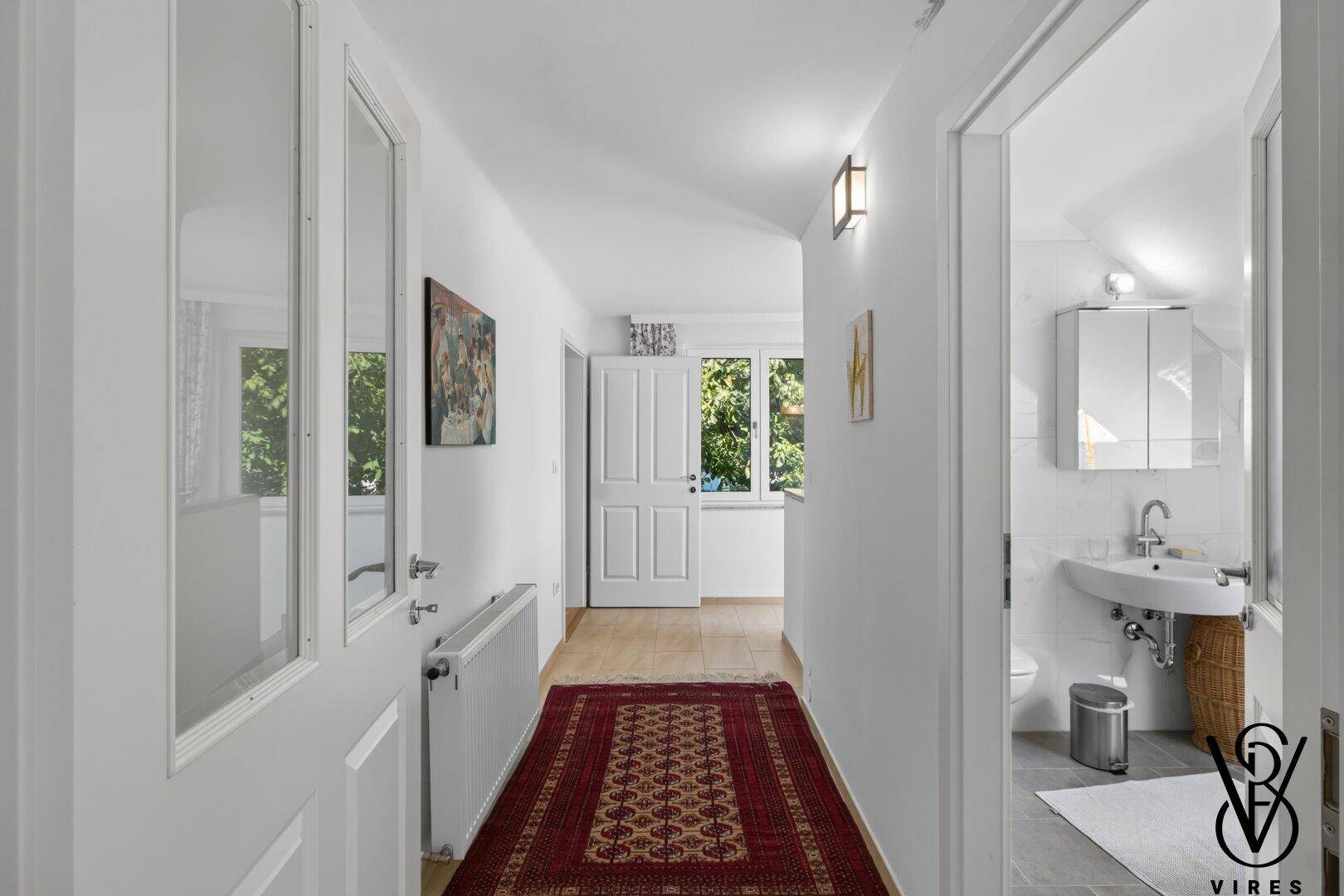 Heller Flur mit Teppichläufer und Zugang zu weiteren Räumen, inklusive Badezimmer.
