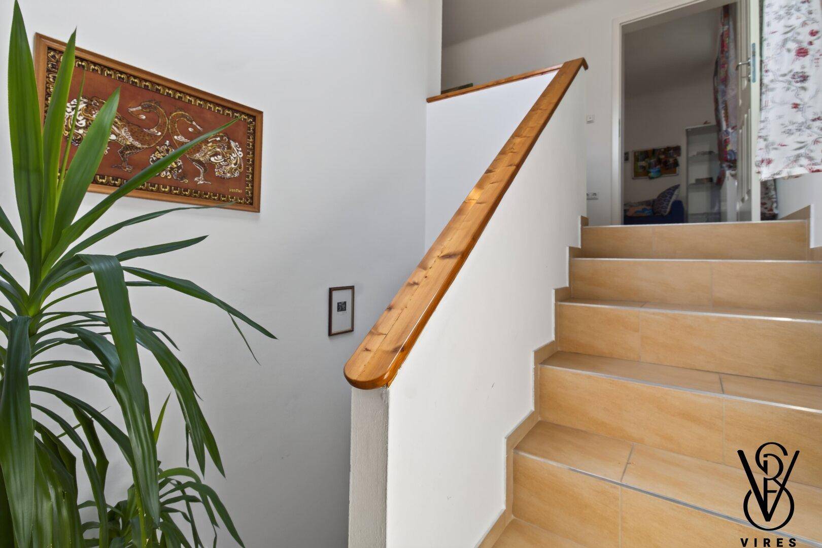 Treppenhaus mit Holzgeländer und heller Gestaltung, verbindet die verschiedenen Etagen des Hauses.