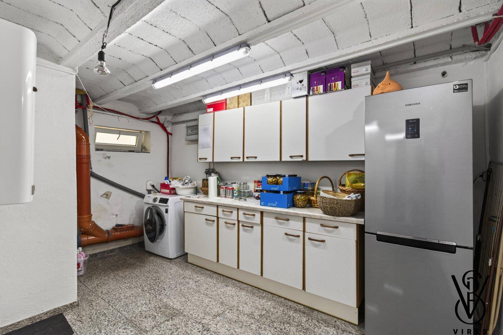 Praktischer Hauswirtschaftsraum im Keller mit Waschmaschine, Kühlschrank und Stauraum.
